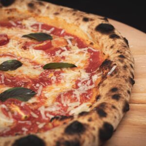 Close-up of a freshly baked Margherita pizza with cheese, basil, and tomato sauce on a wooden board.