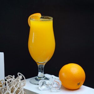 Fresh orange juice served in a glass with ice and a whole orange on a black background.