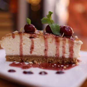 Close-up of a creamy cheesecake slice with cherry topping and mint garnish.